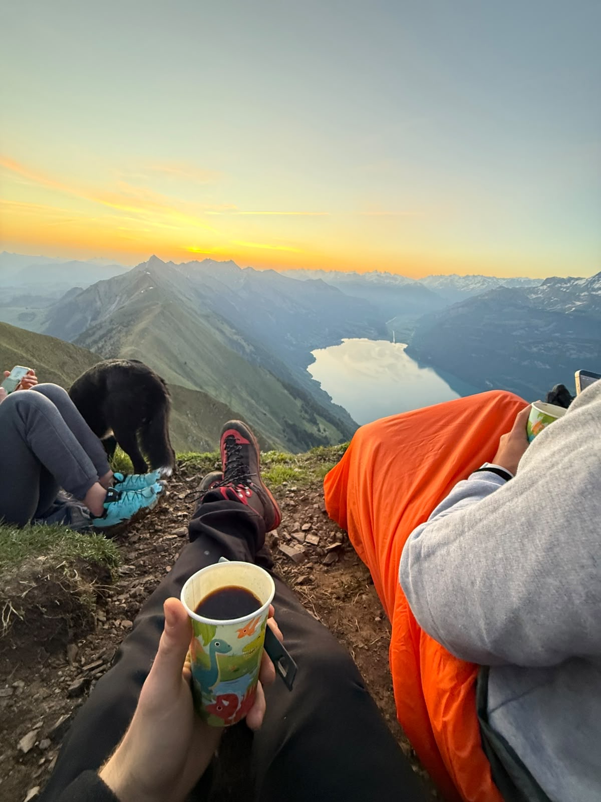 Un café en la mano viendo amanecer sobre el lago, envueltos en la bolsa de dormir